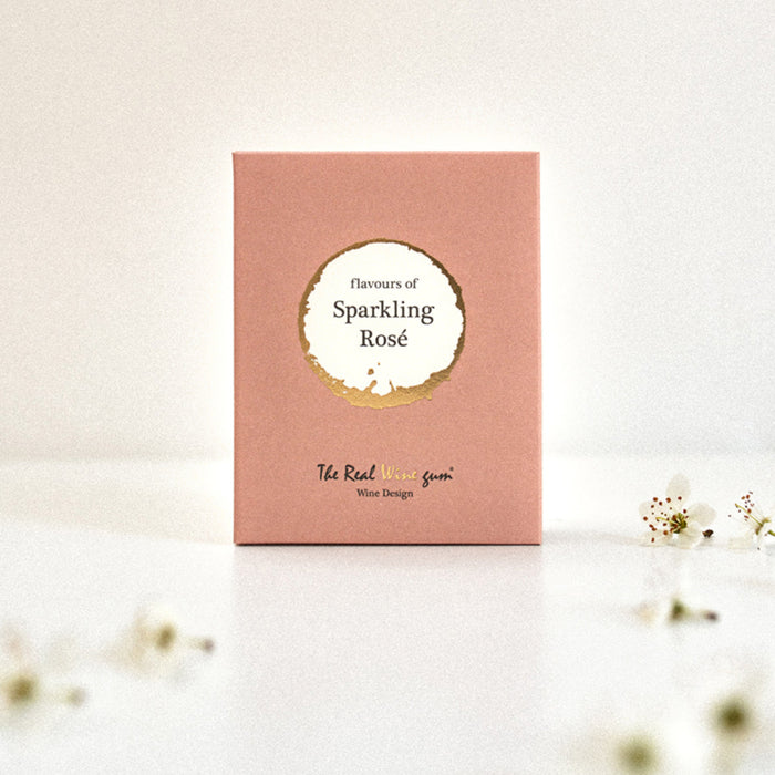 A pink rectangular product box with a circular white and beige label reading 'flavours of Sparkling Rose' and smaller text 'The Real Wine Gum Wine Design,' photographed on a light surface with flowers scattered.