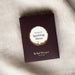 A wine coloured rectangular product box with a circular white and beige label reading 'flavours of Sparkling Shiraz' and smaller text 'The Real Wine Gum Wine Design,' photographed on a light fabric surface.