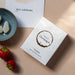 A white rectangular product box with a circular white and gold label reading 'flavours of champagne' photographed on a light fabric surface next to strawberries and a small bowl of gummies.