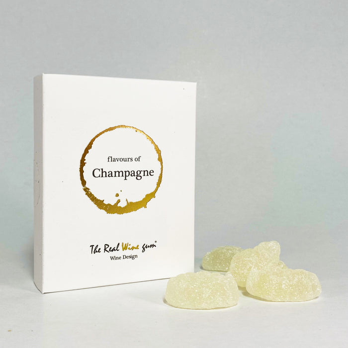 A white rectangular product box with a circular white and gold label reading 'flavours of champagne' photographed on a light surface next to yellow gummies.