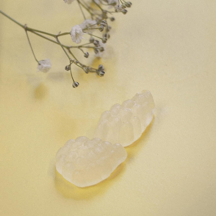 Yellow coloured gummies on a yellow surface next to some flowers.
