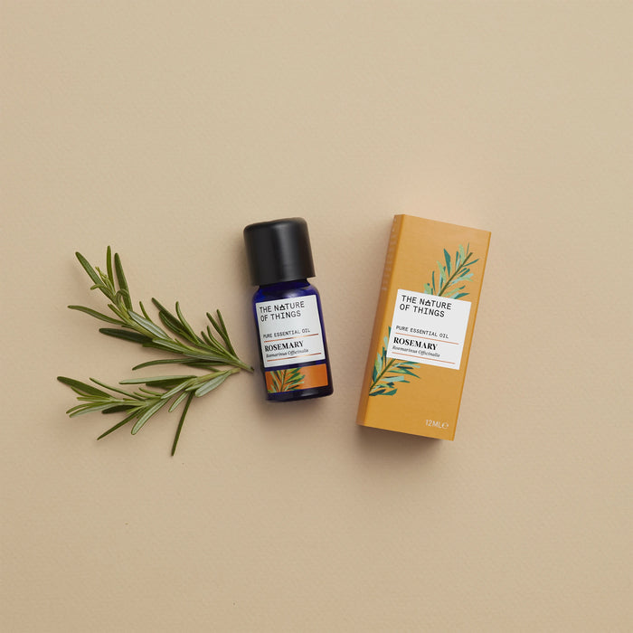 Rosemary essential oil blue bottle beside an orange product box with an illustration of a rosemary leaf on front with rosemary sprig to he left against a pink background