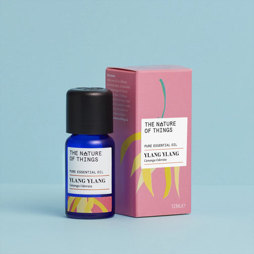 Ylang Ylang essential oil blue bottle beside a pink product box with an illustration of green and yellow plant on front against a blue background