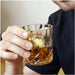 Man's hand holding a whiskey glass with whiskey and a whiskey ball inside.